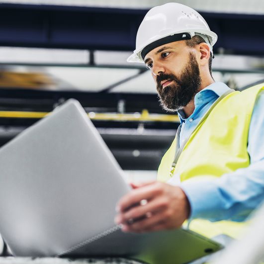 Engineer with hard hat and vest looking at laptop